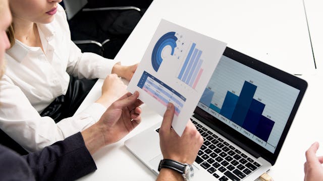 two people looking at graphs and charts on an open laptop and a piece of paper